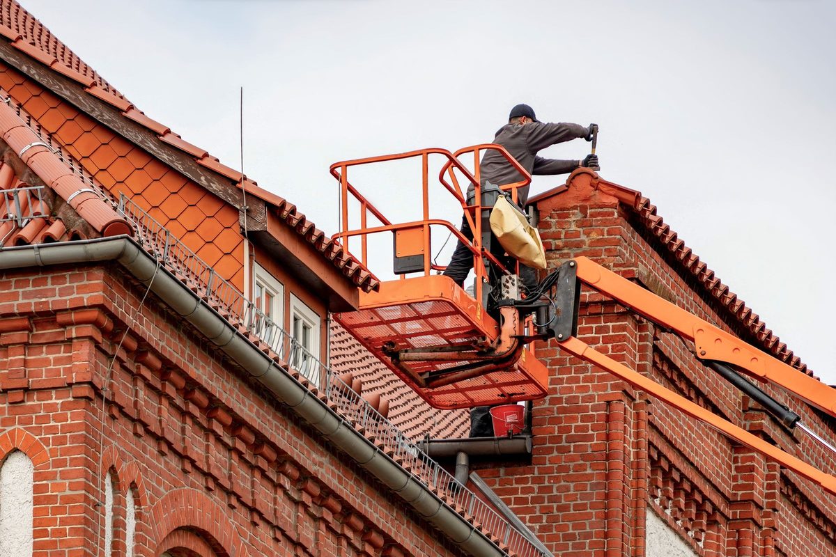 Worker on an aerial lift at the roofline of a red brick building