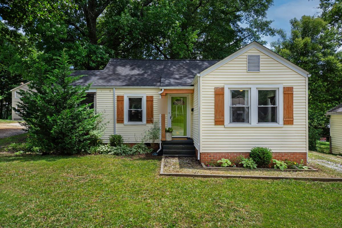 Small one-story cottage with pale yellow siding, wood shutters and a louvered gable vent