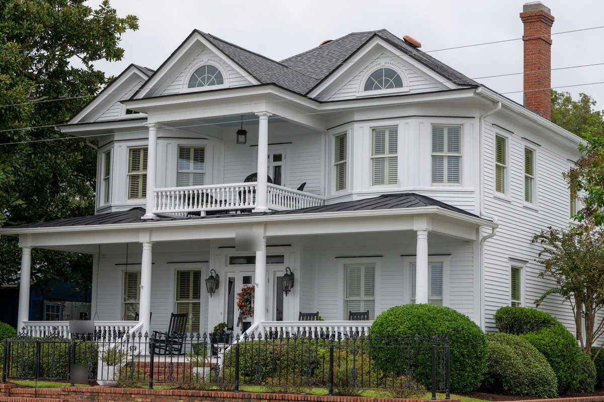 White two-story house with a double front porch, rocking chairs and an iron fence